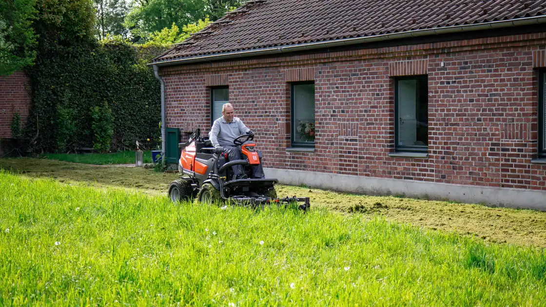 Ein Mitarbeiter beim Rasenmähen vor einem Haus
