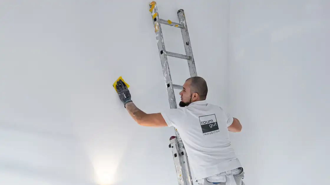 Ein Maler von raumgut steht auf einer Leiter und bessert eine Wand aus
