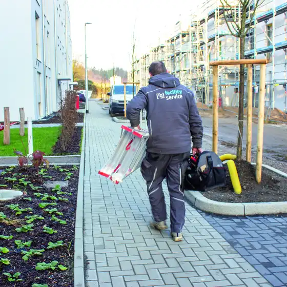 Ein Mann läuft mit Leiter und Arbeitstasche einen Weg entlang