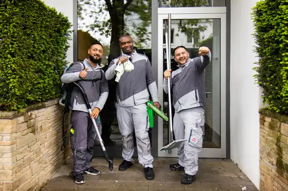 Drei gut gelaunte Mitarbeiter des raumgut Facility Teams stehen zusammen vor einem Hauseingang und lachen in die Kamera.